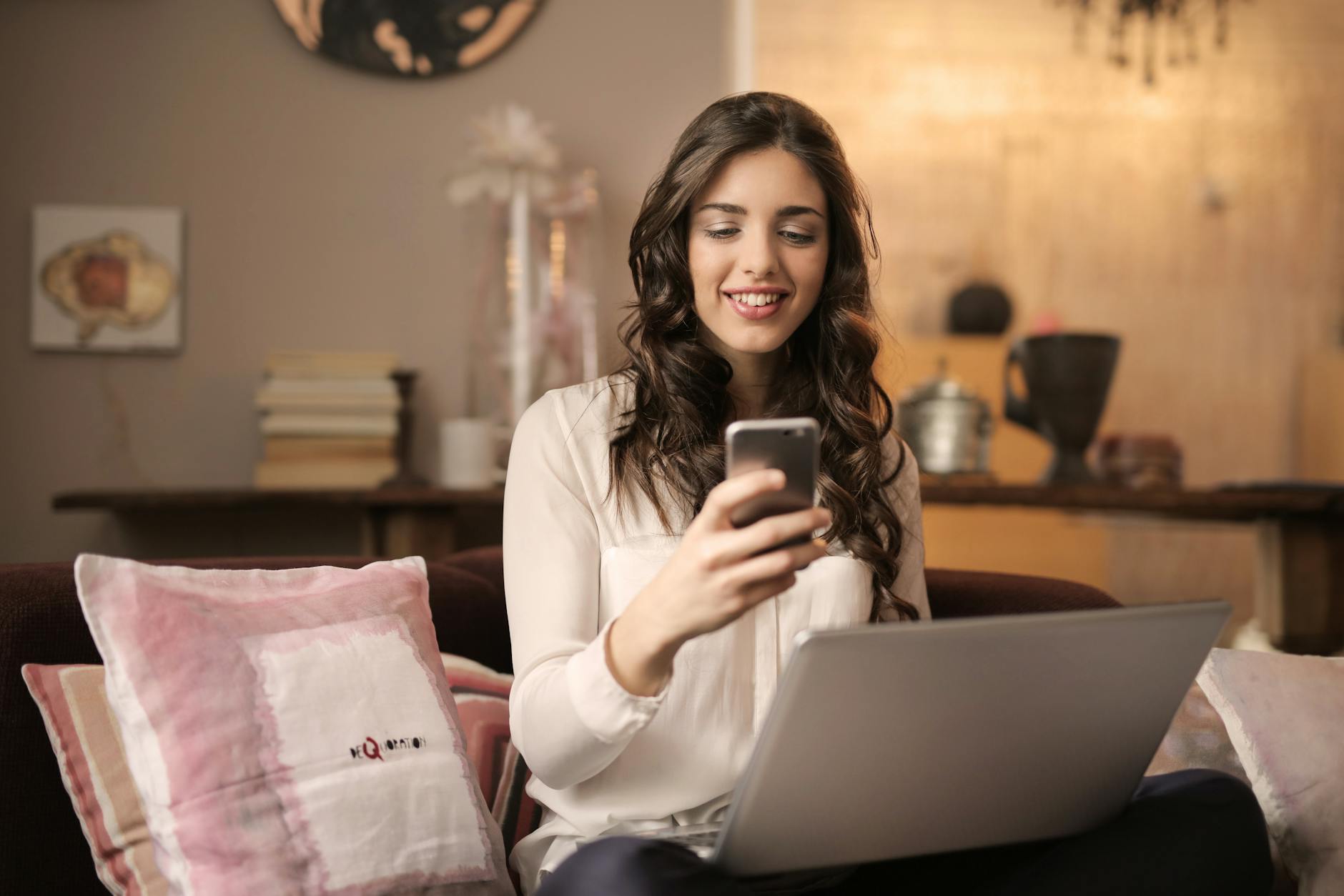 3-strategie-efficaci-con-donna-seduta-sul-divano-che-guarda-il-telefono-con-il-laptop-sulle-gambe 